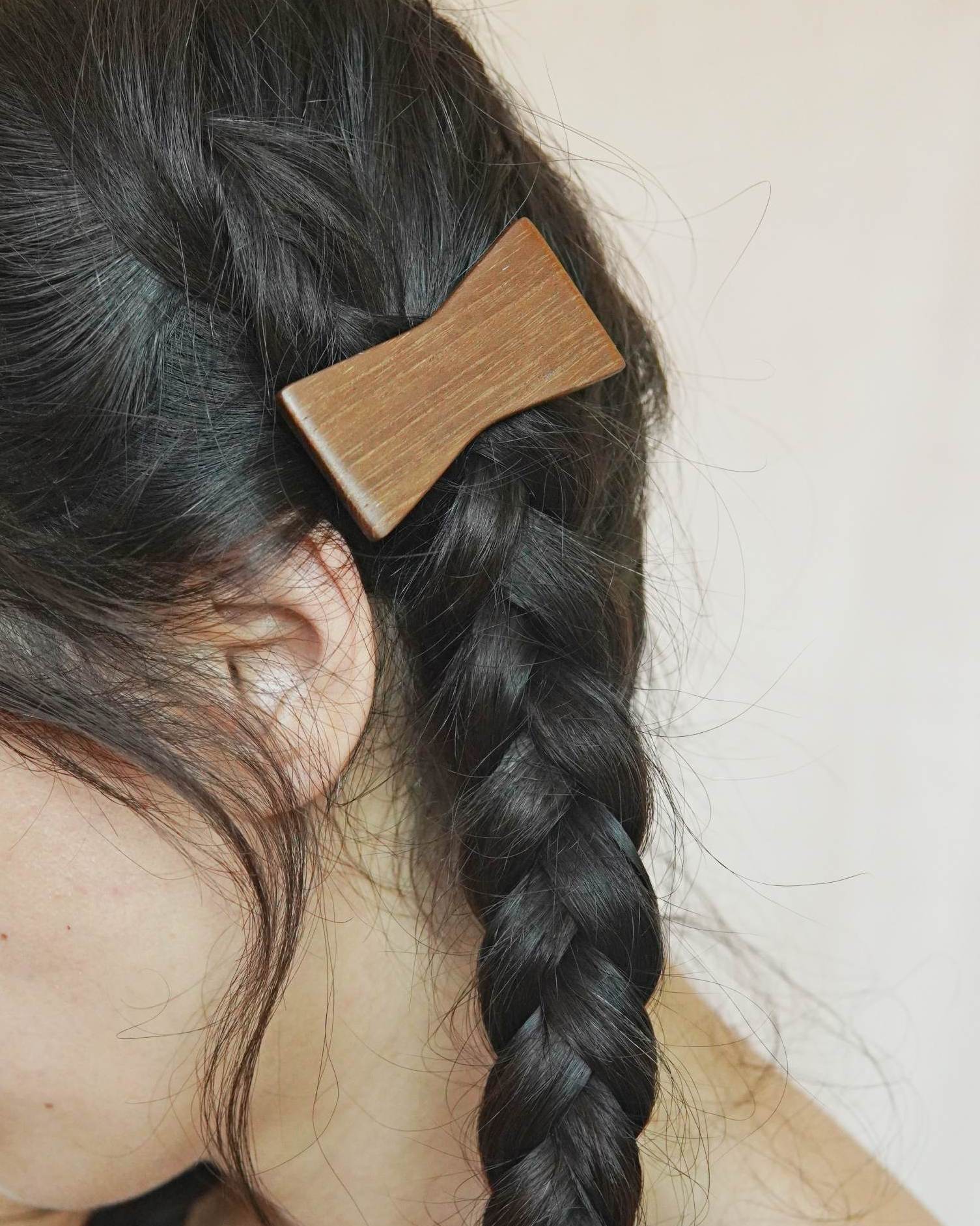 Wooden hair clip in a braided hairstyle on a neutral background.
